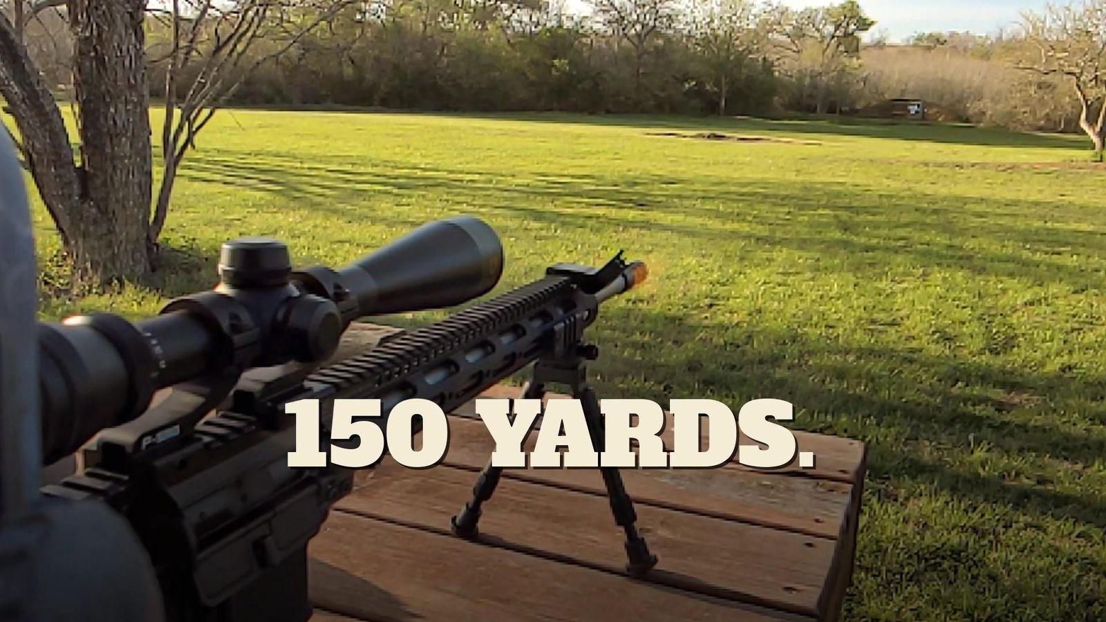 Muzzle flash from the rifle on its bipod, aimed downrange at a target 150 yards across an open field.